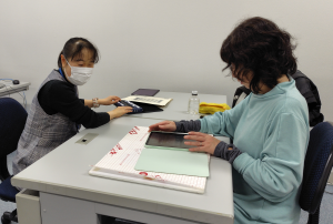 iPad個別講習の写真。机に向かって対面で講習している様子を横からとらえています。右側に受講者、左側に講師の幸田が座っています。