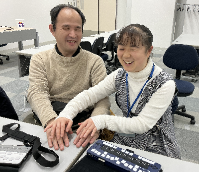 指点字で会話する二人 写真:大阪府ITステーションにて指点字により会話している様子。左が九曜さん、右が幸田。